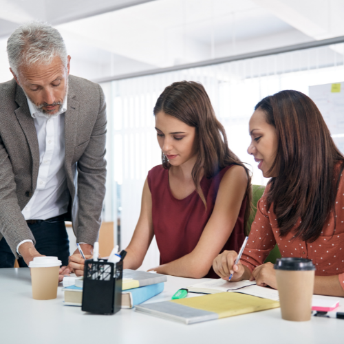Three office workers are reviewing a document at a conference table.