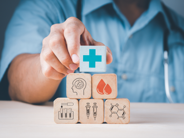 A doctor placing a block with a medical cross symbol on top of a stack of other blocks. The wooden blocks contain various medical symbols.