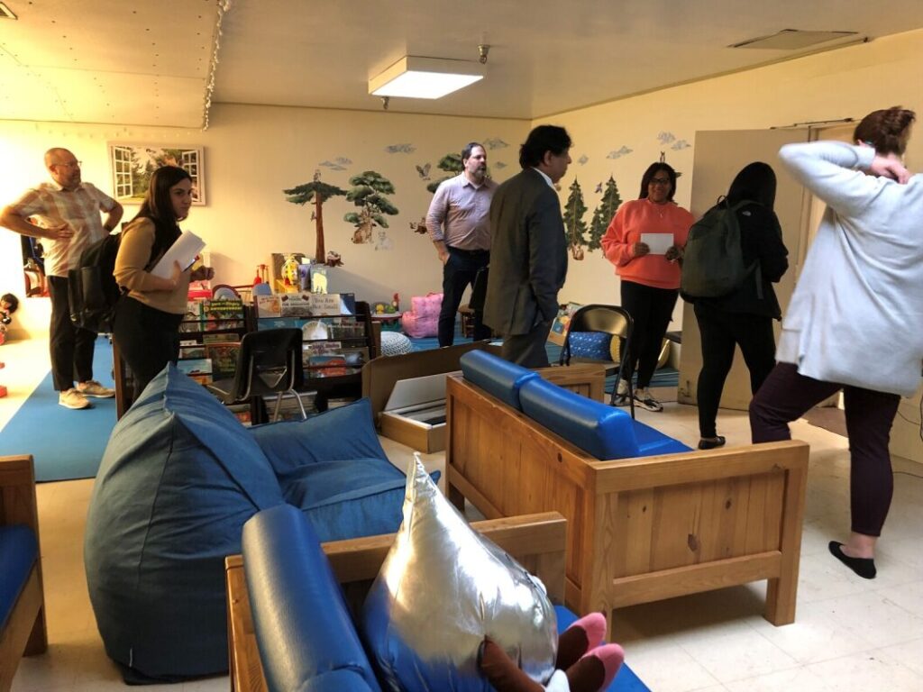 Michigan representatives visiting a Philadelphia supportive housing residence. There are blue couches and paintings of trees on the walls. 