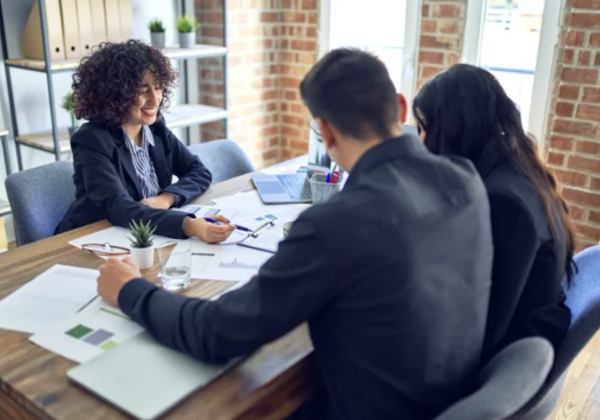 Three office workers sitting around a conference table discussing documents found on the table.