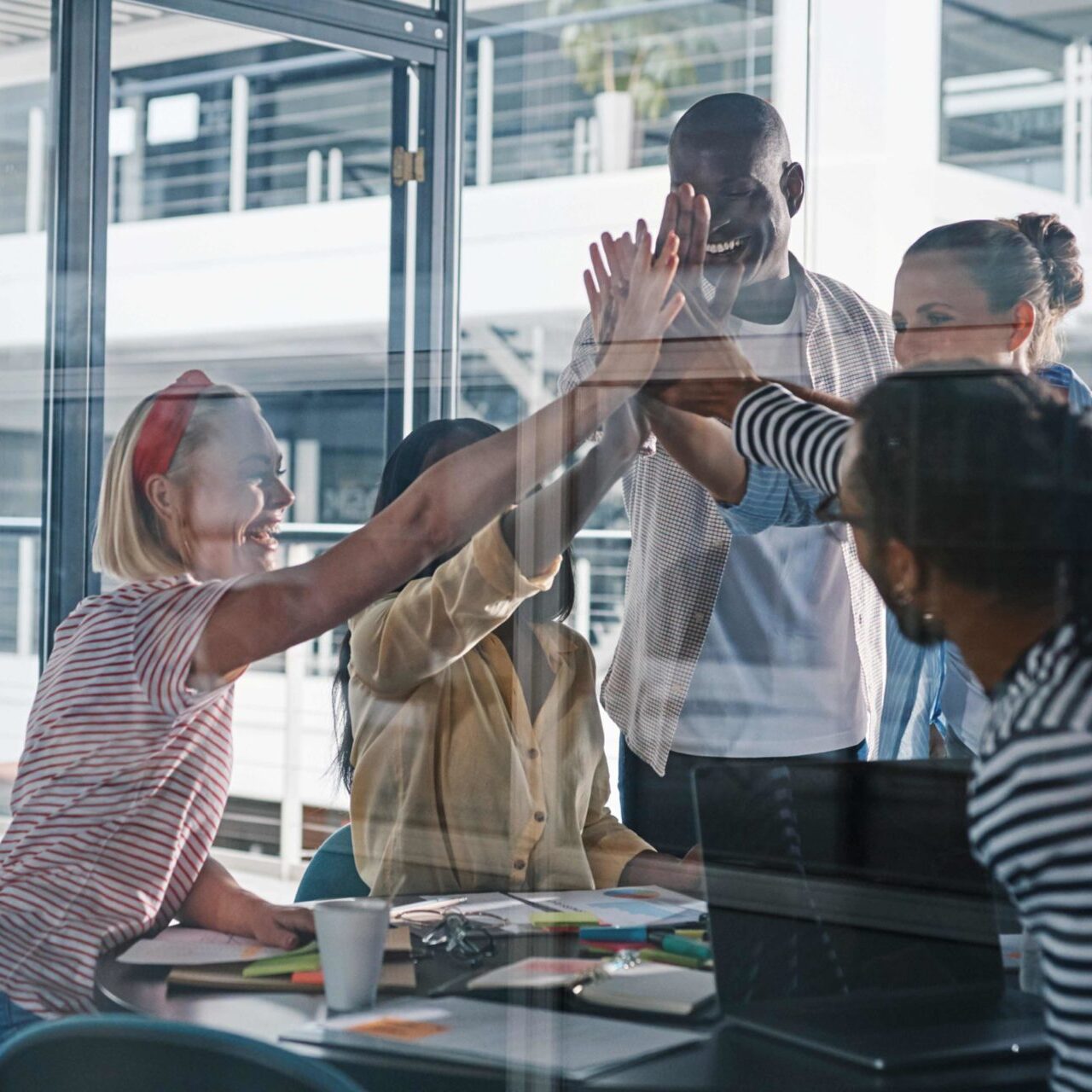 Five young people hi fiving behind office glass door