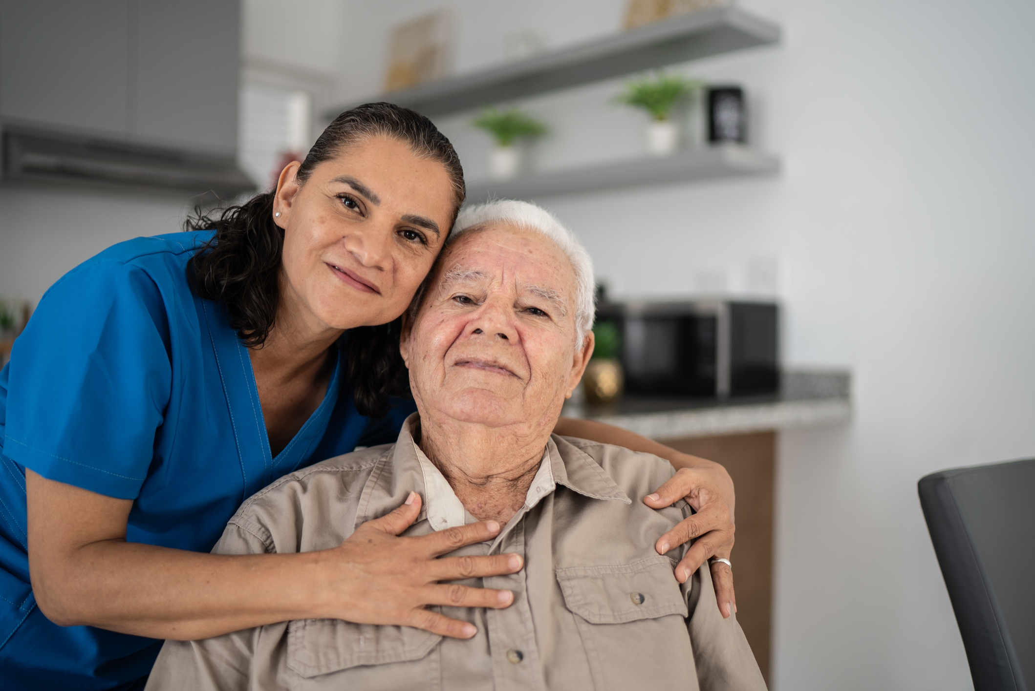 a woman caretaker hugging an older man, both smiling for a photo