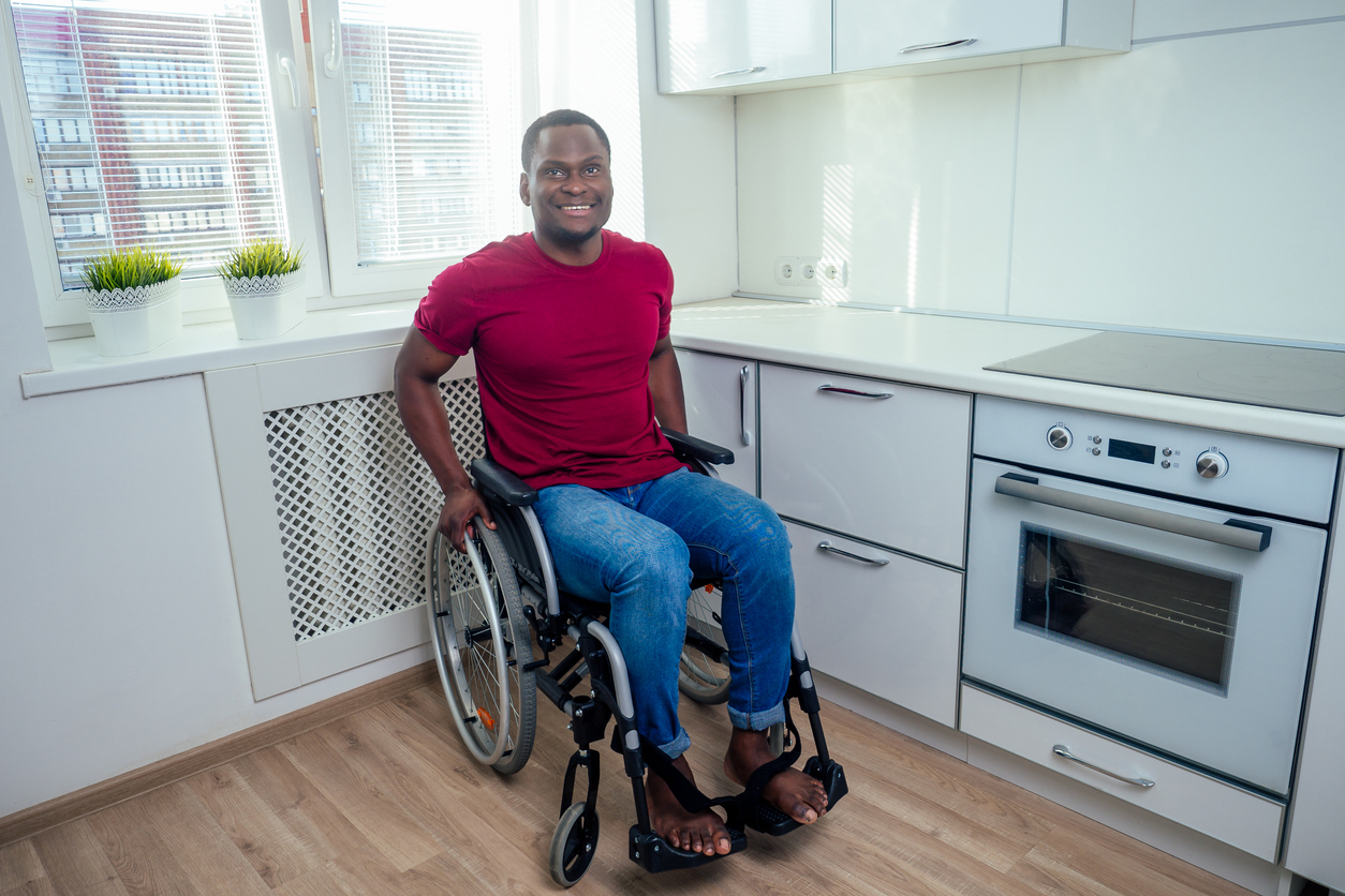 A man smiling in a wheelchair sitting in the kitchen of his new apartment.