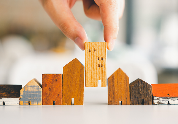 Hand choosing mini wood house model from model and row of coin money on wood table, selective focus,