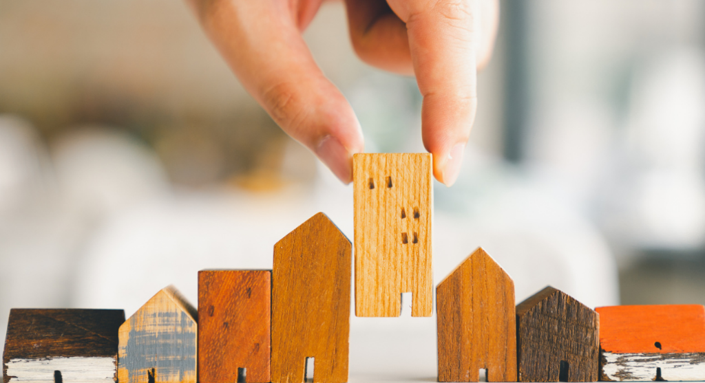 Hand choosing mini wood house model from a row of wooden houses on a table.